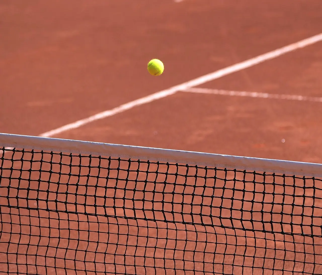 Tennisbold over et net på en grusbane