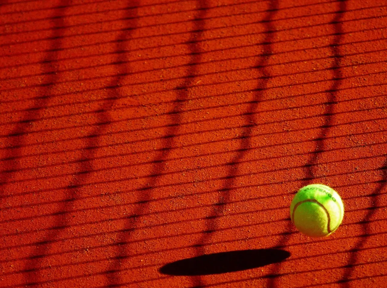 Tennisbold på rød grusbane med skygger