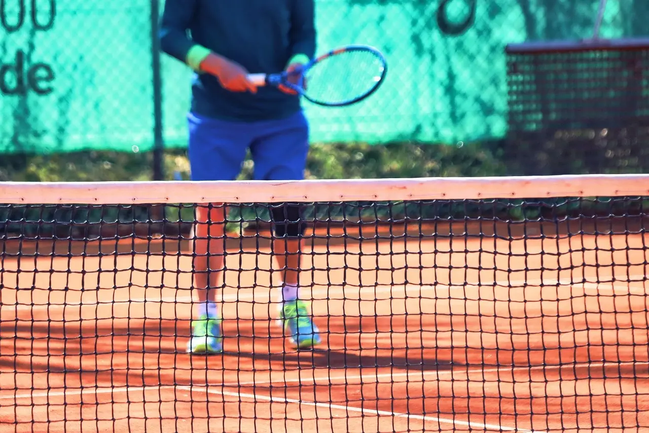 Tennisspiller på grusbane set gennem nettet